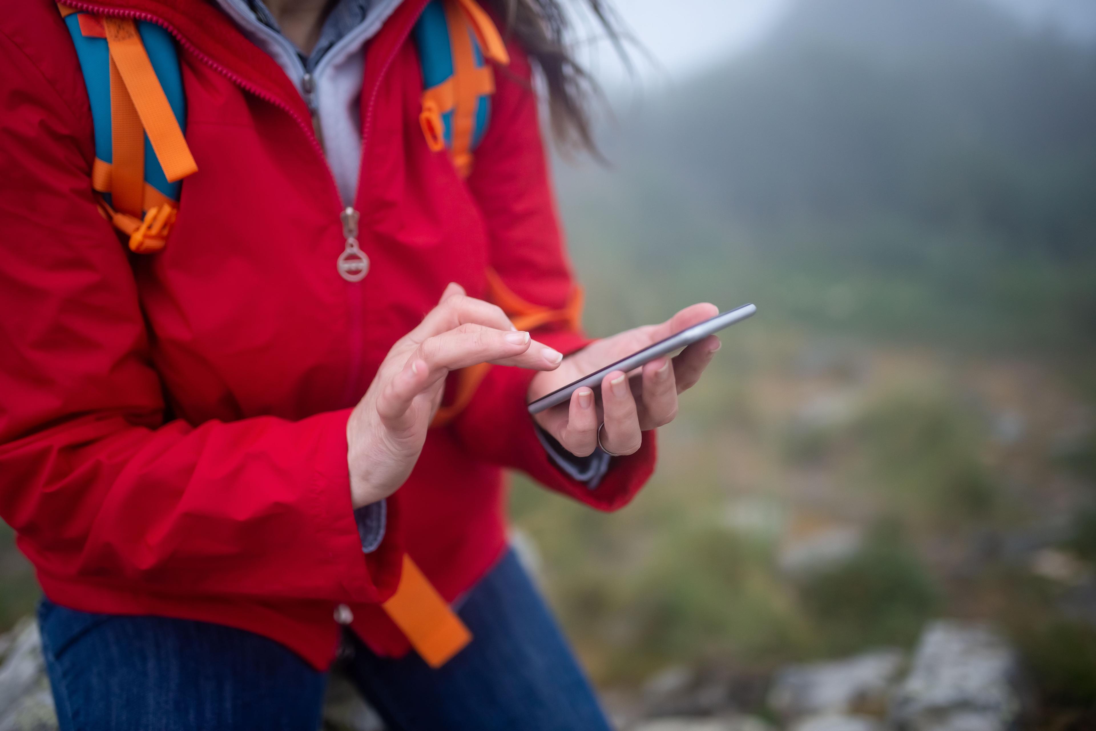 Traveler in a red jacket checking her phone on a foggy hiking trail