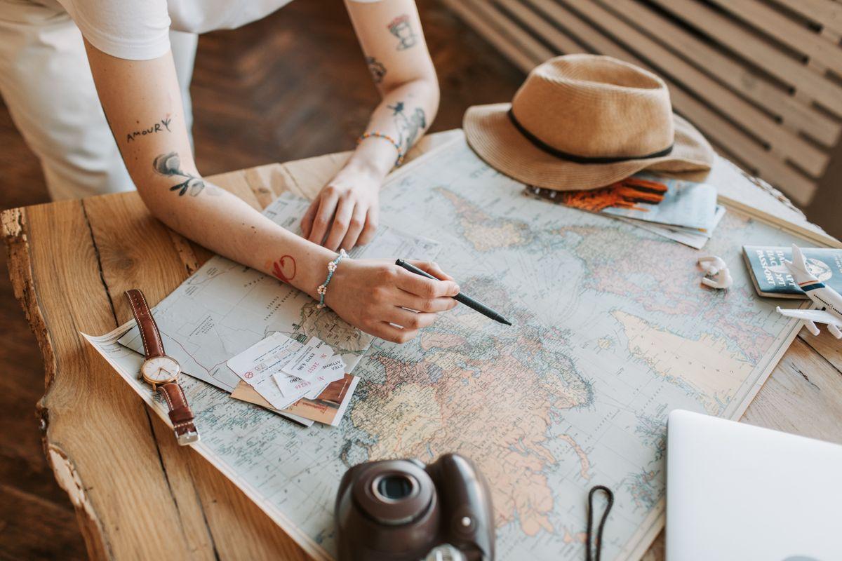 Woman planning a trip with a world map, passports, and travel essentials on a wooden table